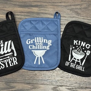May include: Three black and blue oven mitts with white text and images. The mitts feature the phrases "The Grill Master", "Grilling and Chilling", and "King of the Grill".