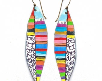 May include: A pair of colorful, hand-painted earrings shaped like teardrops. The earrings feature a white background with stripes of pink, blue, yellow, green, and orange. The earrings are accented with black lines and scribbles.