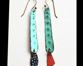 May include: A pair of long, turquoise earrings with a textured surface. Each earring has a small, red and black pendant hanging from the bottom.