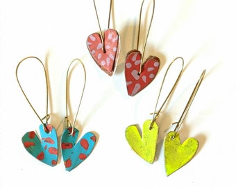 May include: Four pairs of heart-shaped earrings with different patterns. Two pairs are red with white polka dots, one pair is turquoise with red polka dots, and one pair is yellow.