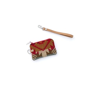 May include: A small, rectangular coin purse with a geometric pattern in red, brown, and beige. It has a zipper closure and a small metal ring. A separate tan leather wrist strap with a silver-tone clasp is also included.