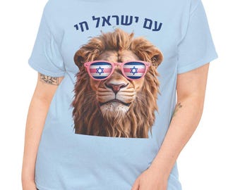 Op de afbeelding: Een lichtblauw T-shirt met de Hebreeuwse tekst "עם ישראל חי" en een leeuw die een roze zonnebril draagt met het patroon van de Israëlische vlag.