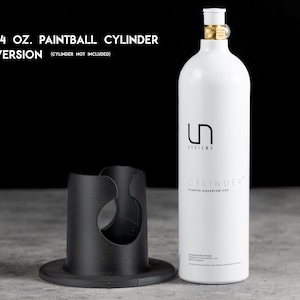 以下が含まれることがあります： 黒いベースと黒いシリンダーホルダーが付いた、白い710 mlペイントボールシリンダー。シリンダーには「UN SYSTEMS CYLINDER」の文字が印刷されています。「24 OZ. PAINTBALL CYLINDER VERSION (CYLINDER NOT INCLUDED)」の文字も表示されています。