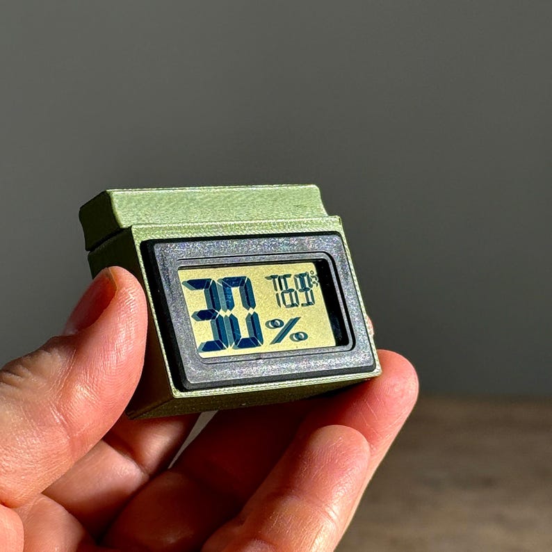 May include: A small, green, digital hygrometer with a black display showing a humidity reading of 30%.