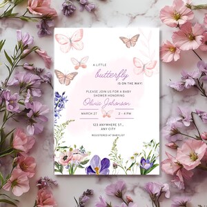 May include: A baby shower invitation with a watercolour design. The invitation features butterflies and floral elements in shades of pink, purple, and green. The text reads "A little butterfly is on the way!" and includes the date, time, and location.