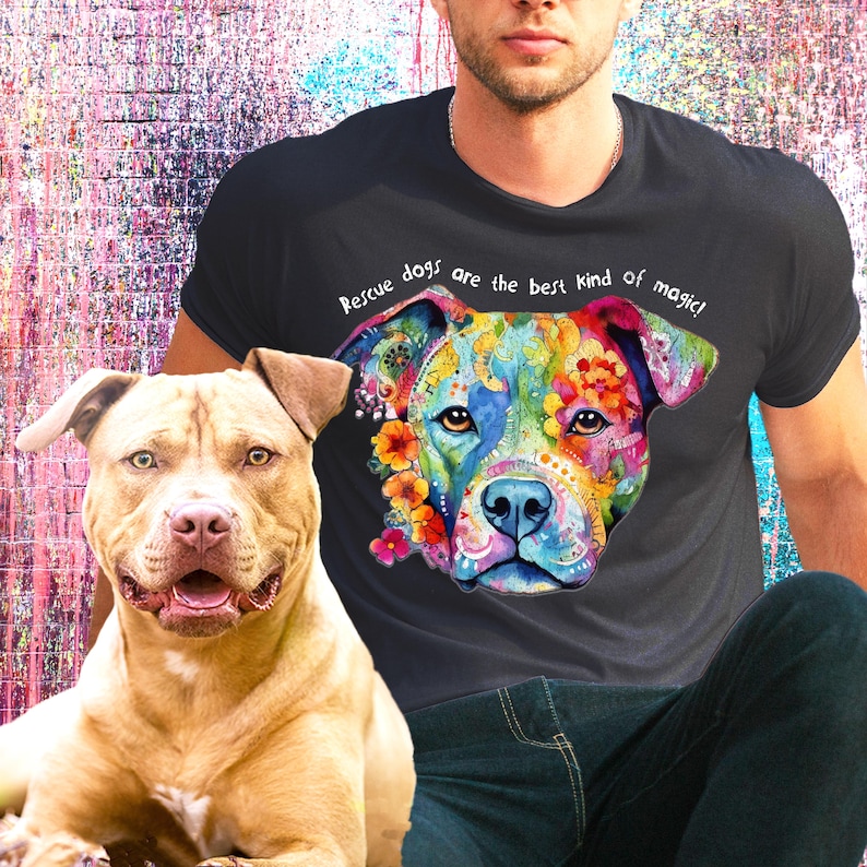以下が含まれることがあります： 黒いTシャツを着た人が、犬のカラフルなイラストと「レスキュー犬は最高の魔法です！」という文字をプリントしています。茶色と黄褐色のピットブルテリアが前景に座っています。