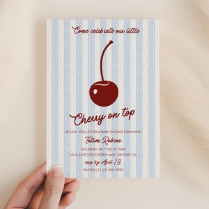 May include: A baby shower invitation with a blue and white striped background. The invitation features a red cherry with the text "Cherry on top" and the words "Please join us for a baby shower honoring Tatum Robins". The invitation also includes the date, time, location, and RSVP information.