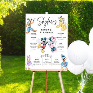 May include: A personalised second birthday sign on an easel, featuring Disney characters like Mickey and Minnie Mouse, Goofy, Pluto, and Donald Duck. The sign includes the name "Skylar's", height, weight, activities, favourite things, and nickname.