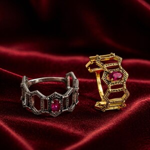 May include: Two rings with geometric designs and ruby gemstones. One ring is silver-toned, and the other is gold-toned. The rings are displayed on a deep red velvet surface.