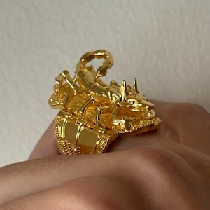 Puede incluir: Un anillo de tono dorado con un dise&ntilde;o de escorpi&oacute;n detallado. El escorpi&oacute;n est&aacute; encaramado sobre una base decorativa, creando un efecto tridimensional.