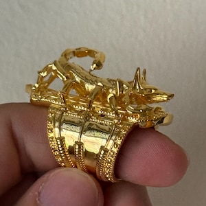 Puede incluir: Un anillo de oro con un dise&ntilde;o detallado que presenta un escorpi&oacute;n y un chacal. El anillo se lleva en un dedo.