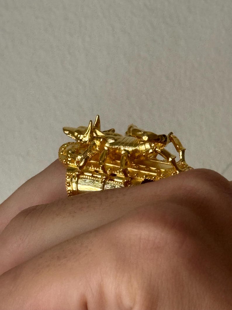 Puede incluir: Un anillo de tono dorado con un dise&ntilde;o de escorpi&oacute;n detallado. El escorpi&oacute;n est&aacute; encaramado sobre una base decorativa, creando una pieza de joyer&iacute;a &uacute;nica y llamativa.