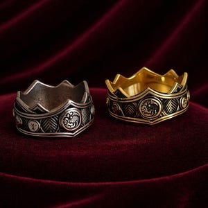 Può includere: Due anelli a forma di corona, uno in metallo color argento e uno in metallo color oro. Ogni anello presenta un bordo superiore frastagliato, una fascia con un motivo a spina di pesce ripetuto e medaglioni circolari con un drago.