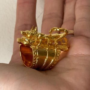 Puede incluir: Un anillo de oro con un dise&ntilde;o detallado de un escorpi&oacute;n y un perro. El anillo es ancho y tiene una banda texturizada.