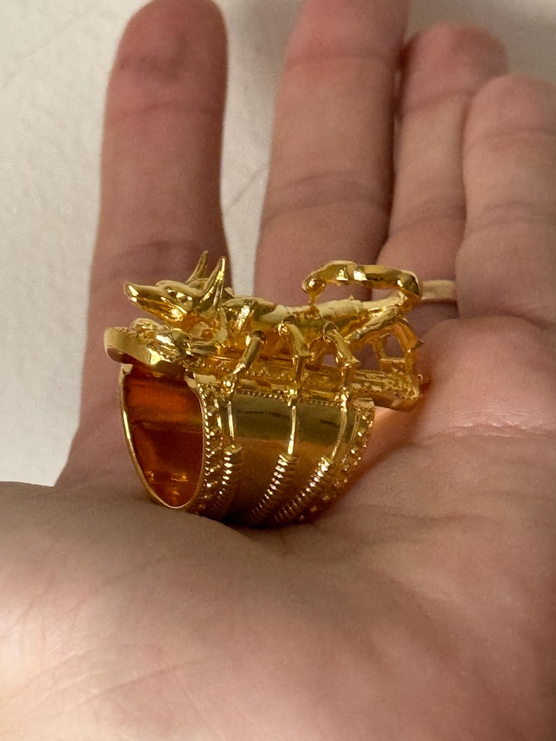 Puede incluir: Un anillo de oro con un dise&ntilde;o detallado de un escorpi&oacute;n y un perro. El anillo es ancho y tiene una banda texturizada.