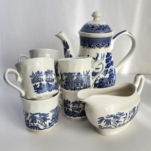 May include: A blue and white Willow pattern tea set. The set comprises a teapot, a milk jug, and several teacups. The blue and white design features a landscape scene. The teacups are stacked, and the set is arranged on a white surface.