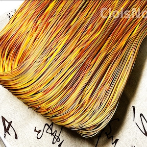 May include: A close-up of a bundle of thin, golden-brown, woven strips of material. The material is arranged in a curved shape, creating a textured, layered effect.