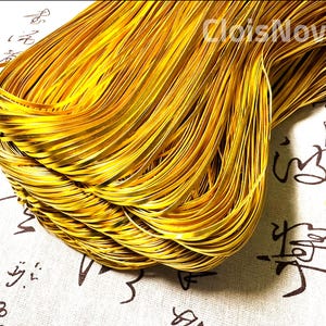 May include: A close-up of a bundle of thin, gold-colored metal wire. The wire is tightly wound together, creating a dense, textured surface.