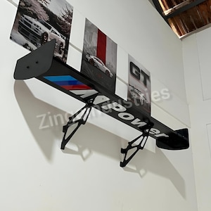 May include: A black car spoiler with the text "Zing Power" in white. The spoiler has a blue, red, and white stripe design. The spoiler is mounted on a white wall with car-themed artwork.
