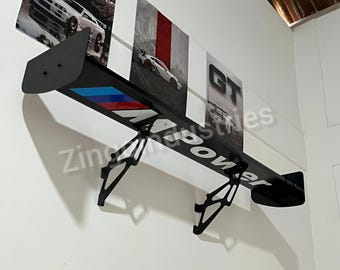 May include: A black car spoiler with the text "Zing Power" in white. The spoiler has a blue, red, and white stripe design. The spoiler is mounted on a white wall with car-themed artwork.