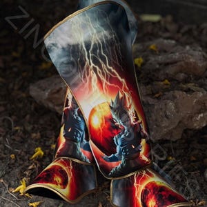 May include: A pair of black and gold shin guards with a graphic print of a cartoon character with a red and yellow aura. The character is surrounded by lightning bolts and a red planet.