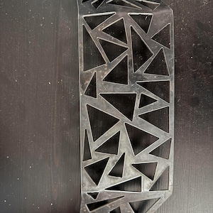 May include: A metal wall decor piece with a geometric design of triangles. The piece is made of dark metal with a rustic finish.