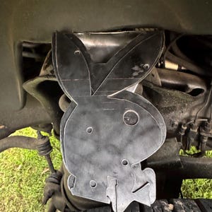 May include: A black metal cutout of a rabbit silhouette, possibly a Playboy bunny, is attached to the underside of a vehicle.