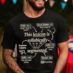 Op de afbeelding: Een zwart t-shirt met een taalkundig diagram in witte en lichtgele tekst. De afbeelding toont de zin This lexicon is syllabically segmented met pijlen die wijzen naar verschillende taalkundige onderdelen zoals Prefix, Suffix en Digraph.