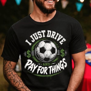 Może przedstawiać: Czarny t-shirt z krótkim rękawem z grafiką piłki nożnej pośrodku. Napis brzmi I JUST DRIVE AND PAY FOR THINGS w kolorze białym, z zielonymi znakami dolara po obu stronach piłki, na tle okrągłego zielonego elementu graficznego.