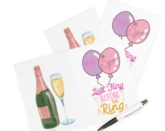 Puede incluir: Tarjetas de felicitación blancas con ilustraciones de botellas de champán, copas y globos. Las tarjetas muestran el texto "Bride to be" y "Last Fling Before the Ring". También hay un bolígrafo blanco con detalles negros.