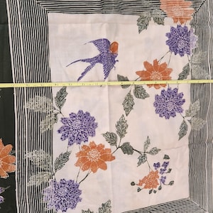 May include: A white fabric with a bird and floral design. The bird is purple and orange, and the flowers are orange and purple. The fabric is bordered by a black and white striped pattern and a dark green border. The fabric measures approximately 18 inches wide.