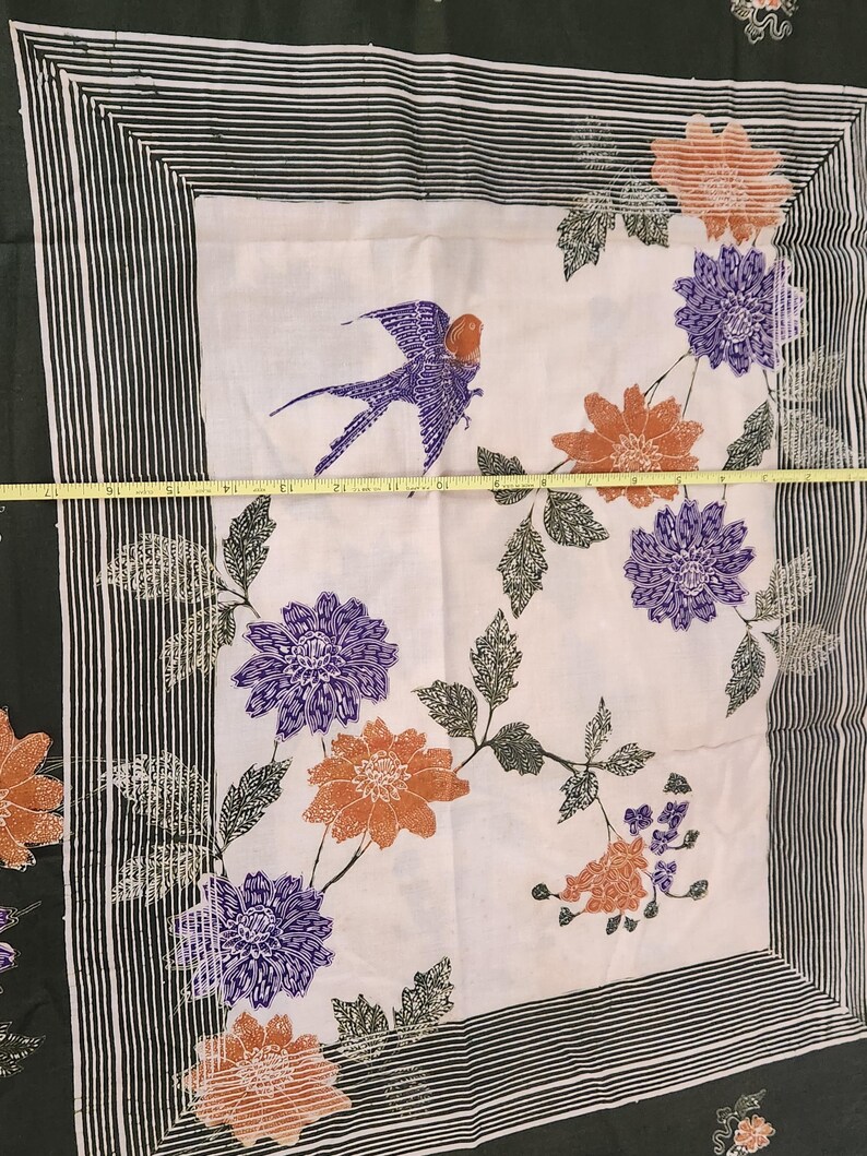 May include: A white fabric with a bird and floral design. The bird is purple and orange, and the flowers are orange and purple. The fabric is bordered by a black and white striped pattern and a dark green border. The fabric measures approximately 18 inches wide.