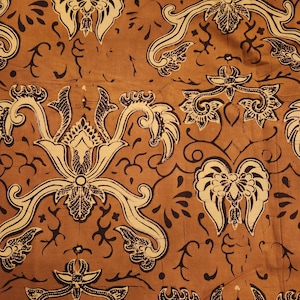 May include: Close-up of a brown fabric with a repeating pattern. The design features cream-colored floral and scroll-like motifs outlined in black. The background is a solid, warm brown color, creating a contrast with the lighter design elements.