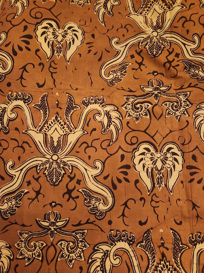 May include: Close-up of a brown fabric with a repeating pattern. The design features cream-colored floral and scroll-like motifs outlined in black. The background is a solid, warm brown color, creating a contrast with the lighter design elements.