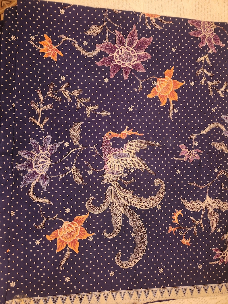 May include: A dark blue fabric with a white polka dot pattern and floral and bird designs in orange, purple, and white. The fabric features a detailed bird in the center and a decorative border along the bottom edge. The overall theme is a textile with an Asian-inspired design.
