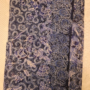 May include: A dark blue fabric with a floral pattern in shades of blue and white. The design features stylized flowers and leaves, with a dark blue border on one side. The fabric appears to be folded or draped.