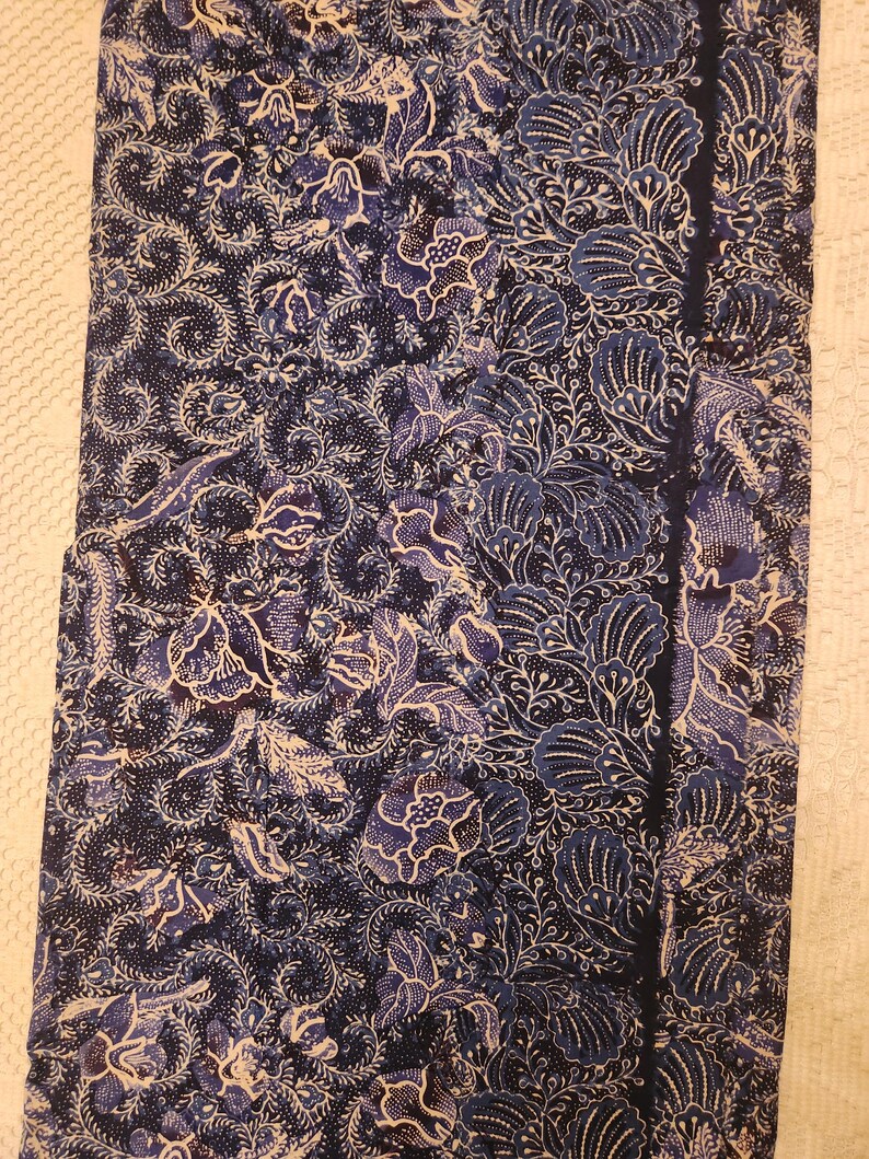May include: A dark blue fabric with a floral pattern in shades of blue and white. The design features stylized flowers and leaves, with a dark blue border on one side. The fabric appears to be folded or draped.