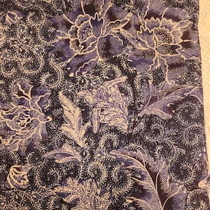 May include: A close-up of a fabric with a floral pattern. The design features large, stylized flowers and foliage in shades of navy blue and white. The fabric has a detailed, textured appearance, with intricate swirls and dots.