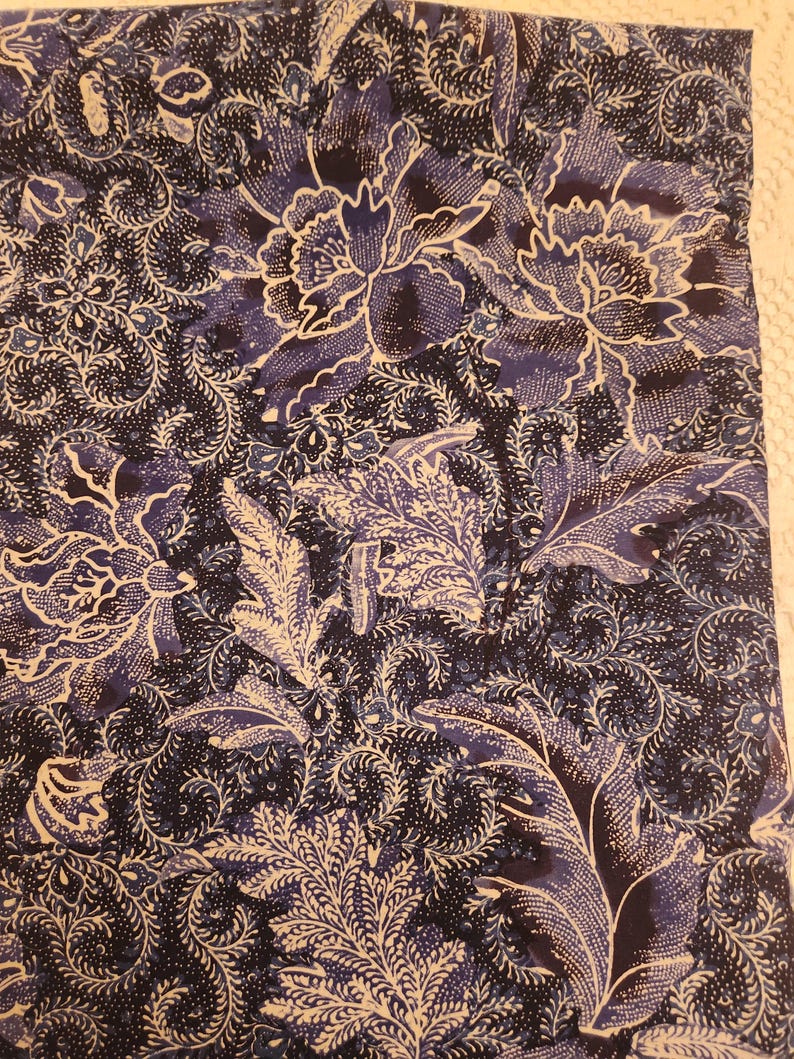 May include: A close-up of a fabric with a floral pattern. The design features large, stylized flowers and foliage in shades of navy blue and white. The fabric has a detailed, textured appearance, with intricate swirls and dots.