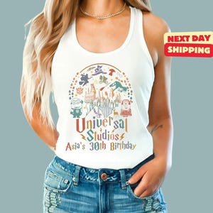 May include: White tank top featuring a colorful graphic of Universal Studios characters and a castle. The text reads "Universal Studios Asia's 30th Birthday". A red and yellow "Next Day Shipping" sticker is visible.