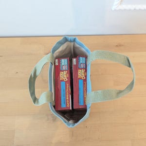 May include: A light blue tote bag with two boxes of Lucky Charms cereal inside. The boxes are red with yellow lettering and a picture of a leprechaun.