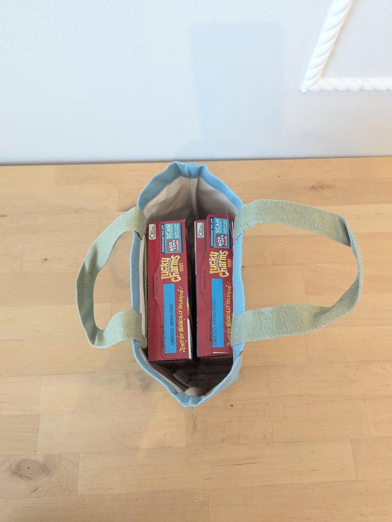 May include: A light blue tote bag with two boxes of Lucky Charms cereal inside. The boxes are red with yellow lettering and a picture of a leprechaun.