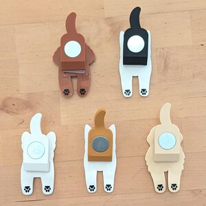 May include: Five different colored dog-shaped magnetic hooks. Each hook is white with a different colored dog body. The dog bodies are brown, black, beige, gold, and white.