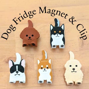 May include: Set of five dog-shaped fridge magnets and clips. The magnets are brown, black, white, orange, and cream. Each magnet features a different breed of dog with a white face and black eyes. The text "Dog Fridge Magnet & Clip" is written in black letters on a white background.