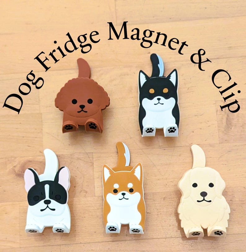 May include: Set of five dog-shaped fridge magnets and clips. The magnets are brown, black, white, orange, and cream. Each magnet features a different breed of dog with a white face and black eyes. The text "Dog Fridge Magnet & Clip" is written in black letters on a white background.