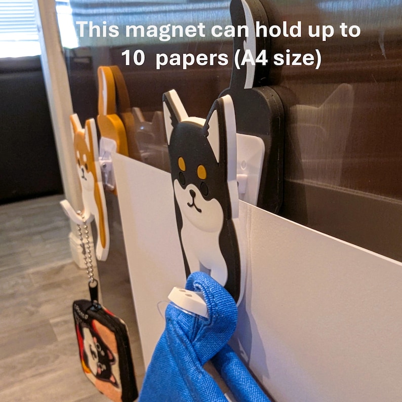 May include: A set of three magnetic hooks shaped like cartoon dogs. The hooks are white with black and brown accents. The text "This magnet can hold up to 10 papers (A4 size)" is visible in the image.