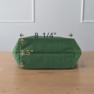 May include: A green fabric tote bag with a measurement of 8 1/4 inches wide and 4.5 inches tall.