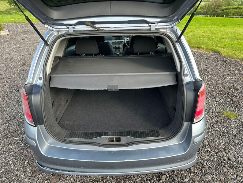 May include: The rear cargo area of a silver hatchback car with the trunk open. The car has a black cargo cover and a black carpet floor.