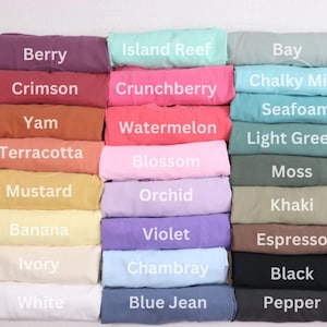 May include: A display of folded fabric in various colors, including Berry, Crimson, and Yam. Each color is labeled with its name in white text. Other colors include Island Reef, Crunchberry, and Chalky Mint. The fabric appears to be soft and comfortable.