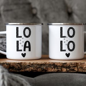 May include: Two white enamel mugs with black lettering. The mugs say "LO LA" and "LO LO" with small hearts around the letters.
